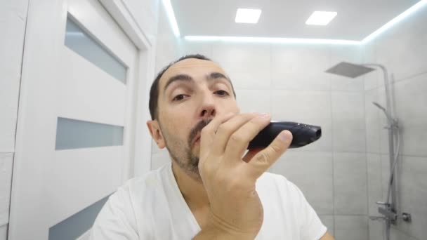 Νεαρός άνδρας ξύρισμα γενειάδα του με ηλεκτρική ξυριστική μηχανή στο μπάνιο — Αρχείο Βίντεο