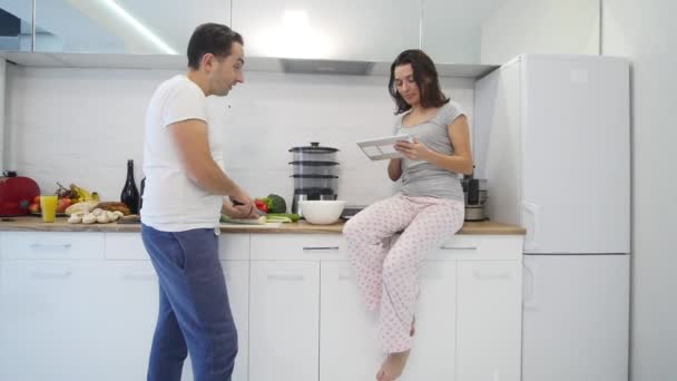 Парочка на домашней кухне. Мужчина готовит салат и женщину с помощью электронных таблеток — стоковое видео