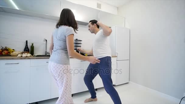 Mattina a casa felice giovane coppia appena sposata ballare ascoltando musica in cucina indossando il pigiama. rallentatore — Video Stock