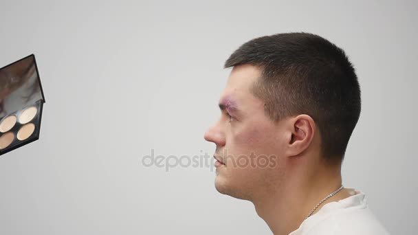 化妆师擦眉毛胡须的中年男子坐在他闭着眼睛用棉垫她擦拭他的皮肤，或者将应用药物治疗 — 图库视频影像