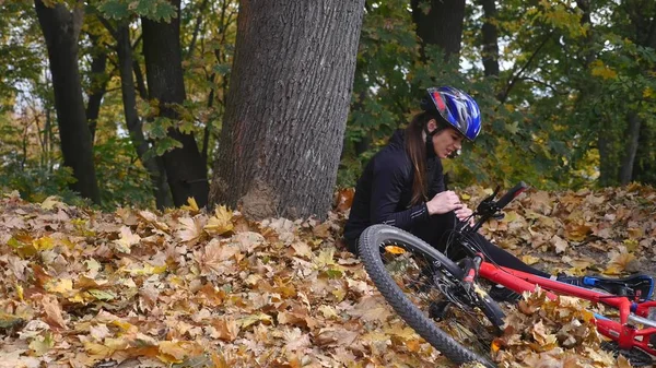Eine junge Frau sitzt nach einem Sturz vom Fahrrad im Park, beruhigt die Schmerzen im Knie, ist eine gefährliche Radtour im Park an einem Herbsttag — Stockfoto
