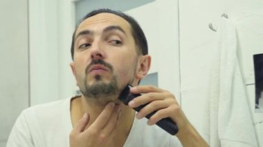 Genç adam banyoda Elektrikli tıraş makinesi ile sakalını tıraş