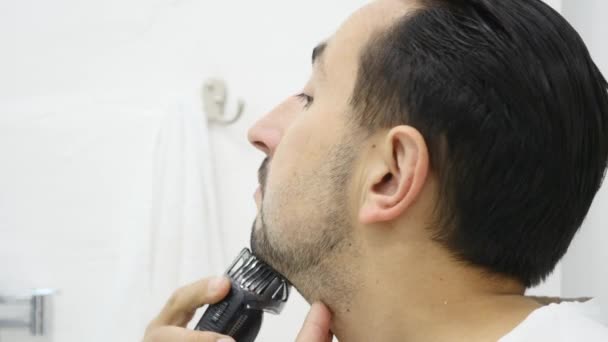 Jovem barbeando sua barba com barbeador elétrico no banheiro — Vídeo de Stock