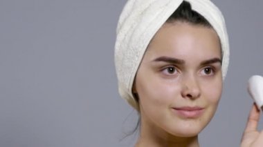 kız temiz ve taze yüzünü yapma. Yüzünü sünger ile silme ve gri arka plan üzerinde izole dururken gülümseyen güzel genç üstsüz kadın. Yakın çekim