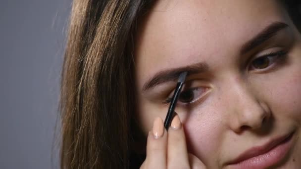 Uma bela jovem penteia a sobrancelha. Mulher bonita desenhar forma de beleza de sobrancelhas usando escova cosmética. Fechar — Vídeo de Stock