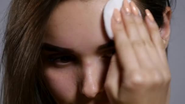 Chica Haciendo su cara limpia y fresca. Hermosa mujer joven sin camisa limpiándose la cara con esponja y sonriendo mientras está de pie aislada sobre un fondo gris. De cerca. — Vídeo de stock