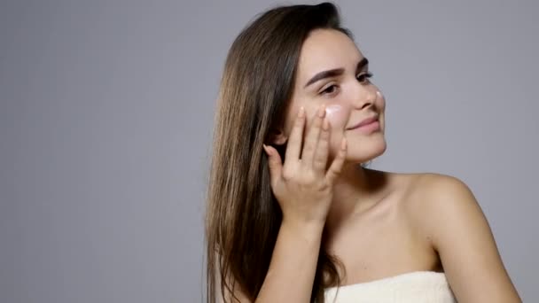 Młoda kobieta piękne stosowania kremu na twarz, na szarym tle — Wideo stockowe