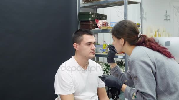 Het meisje maakt aan de man. een professionele make-up artiest make-up een wenkbrauw — Stockvideo