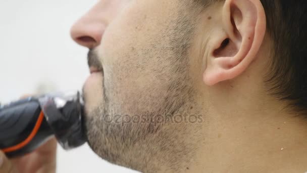 Ung man rakar skägget med rakapparat i badrummet — Stockvideo
