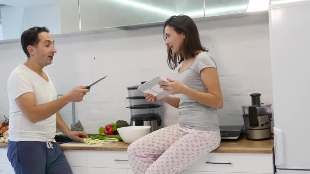 Pareja en la cocina casera. Hombre preparar ensalada y mujer usando tableta electrónica — Vídeo de stock