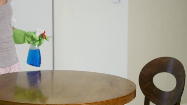 A woman in a tight gray T-shirt with a deep neckline wipes a large kitchen table with a rag — Stock Video