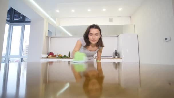 Een vrouw in een strak grijs T-shirt met een diepe decollete veegt een grote keukentafel met een doek — Stockvideo