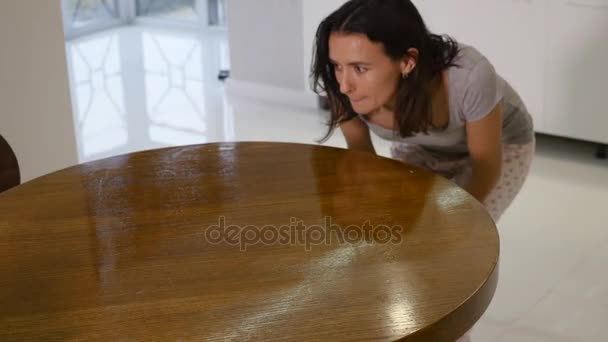 Une femme dans un T-shirt gris serré avec un décolleté profond essuie une grande table de cuisine avec un chiffon — Video