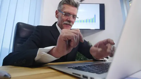 Пожилой бизнесмен, работающий с компьютером в современном офисе — стоковое фото