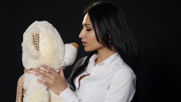 Ein hübsches Mädchen umarmt und küsst einen niedlichen Teddybär. Nahaufnahme, Studio auf schwarzem Hintergrund — Stockvideo