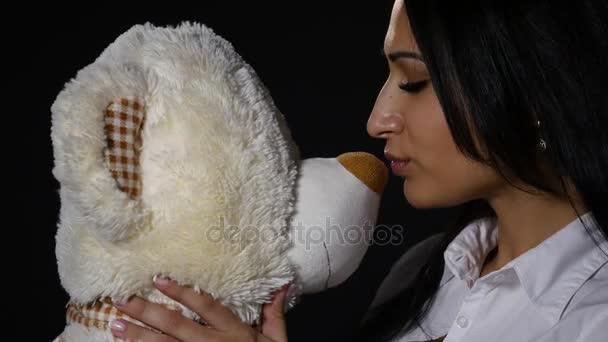 A lovely girl hugs and kisses a cute teddy bear. Close-up shot, studio on black background — Stock Video