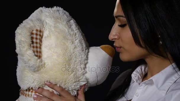 Una chica encantadora abraza y besa a un lindo osito de peluche. Primer plano, estudio sobre fondo negro — Vídeo de stock