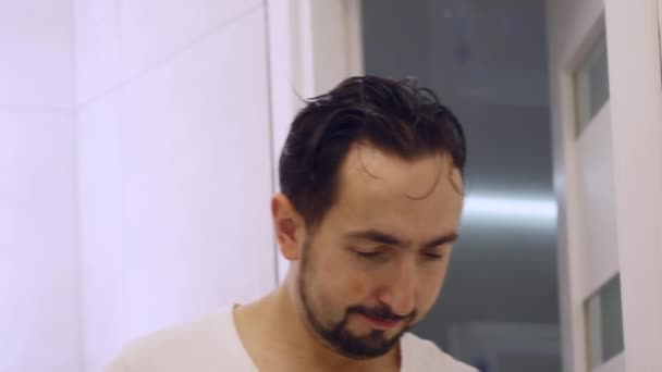 Z bliska. Człowiek myje przed lustrem. Zmęczony zarośnięty facet w biały T-shirt — Wideo stockowe