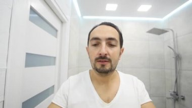 Genç adam banyoda Elektrikli tıraş makinesi ile sakalını tıraş