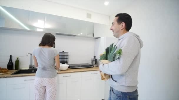 Жінка на кухні готує їжу і чоловік приносить продукти — стокове відео