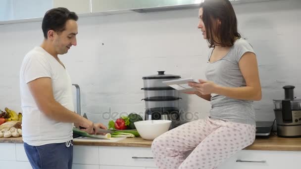 Pareja en la cocina casera. Hombre preparar ensalada y mujer usando tableta electrónica — Vídeos de Stock