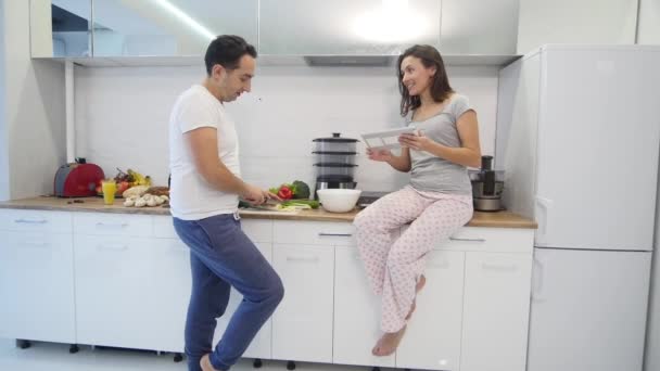 Pareja en la cocina casera. Hombre preparar ensalada y mujer usando tableta electrónica — Vídeo de stock