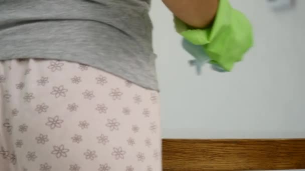 En kvinna i en tight grå T-shirt med djup ringning våtservetter ett stort köksbord med en trasa — Stockvideo