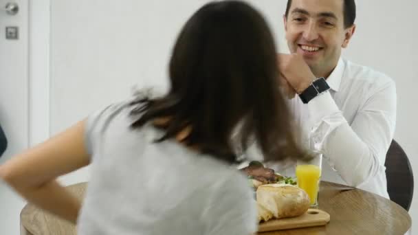 Casal feliz conversando e tomando café da manhã juntos em casa na cozinha — Vídeo de Stock