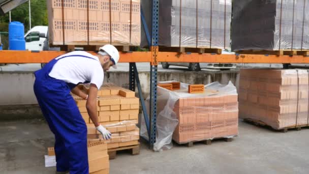 Arbeiter im Lager prüfen rote Ziegel, die zu Würfeln gestapelt sind. rote Ziegelsteine auf Lager. Lagerbausteine. Ziegeleiprodukte lagern. rote Ziegel, in Blöcken gelegt, die durch transparente Verpackungen geschützt sind. — Stockvideo