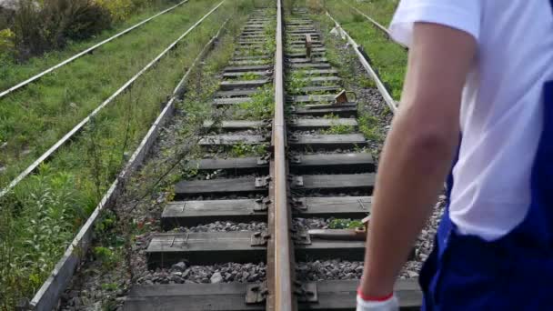 Железнодорожный рабочий в белом шлеме идущий вдоль железной дороги — стоковое видео
