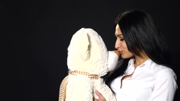 Una bella ragazza abbraccia e bacia un simpatico orsacchiotto. Primo piano, studio su sfondo nero — Video Stock