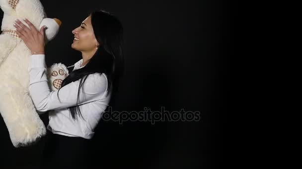 Милая девушка обнимает милого плюшевого мишку. Крупный план, студия на черном фоне — стоковое видео