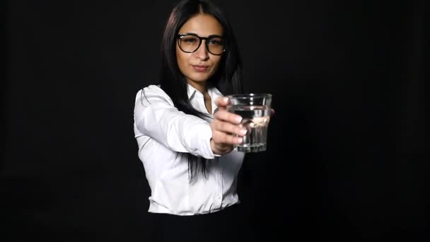 Young beautiful girl holding a glass of water on black background — Stock Video