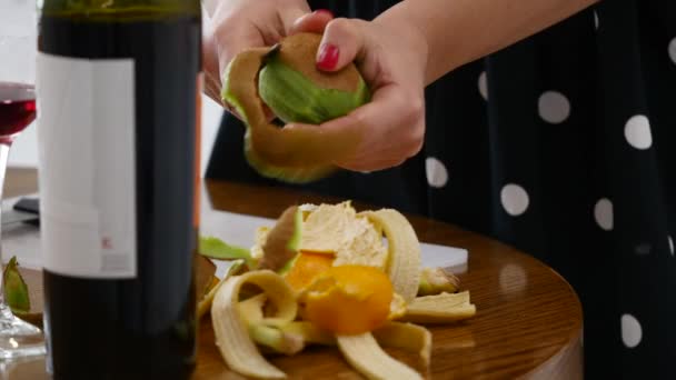 Leuk meisje zitten op de keukentafel en peeling kiwi vruchten — Stockvideo