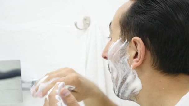 Мужчина наносит пену для бритья на кожу лица, кожу и гигиену, утренний ритуал — стоковое видео