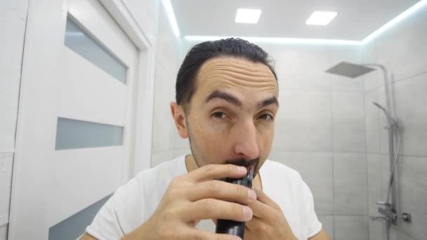 Joven afeitándose la barba con afeitadora eléctrica en el baño — Vídeos de Stock