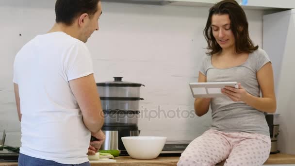 Ζευγάρι στην κουζίνα στο σπίτι. Ο άνθρωπος προετοιμασία σαλάτα και γυναίκα με τη χρήση ηλεκτρονικής ταμπλέτας — Αρχείο Βίντεο
