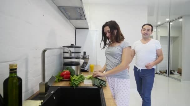 Tipo cariñoso abrazando a su novia sonriente en su cocina temprano en la mañana con el desayuno se hace en cámara lenta — Vídeos de Stock