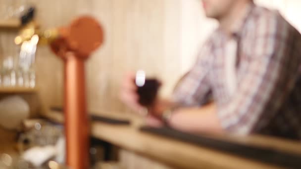 O jovem bebe cerveja atrás de um balcão de bar. Foco seletivo — Vídeo de Stock