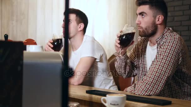 Два молодых человека сидят в баре и разговаривают друг с другом, когда пьют пиво. — стоковое видео