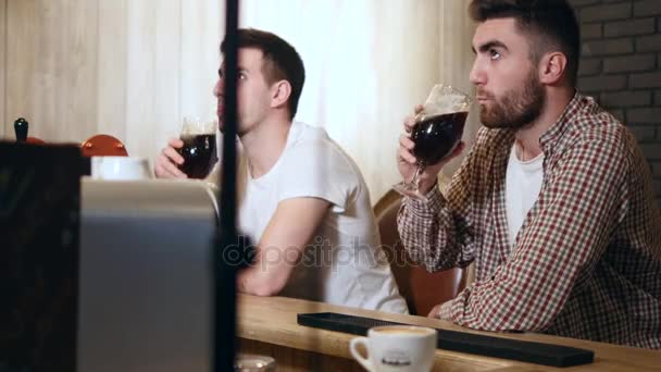 Dos jóvenes amigos sentados en el bar y hablando entre sí mientras beben cerveza — Vídeos de Stock