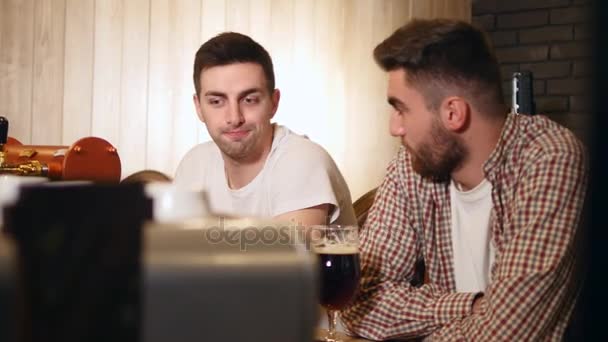 Zwei befreundete junge Männer sitzen in der Bar und unterhalten sich beim Biertrinken — Stockvideo
