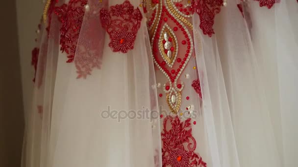 Белые с красной вышивкой свадебные платья висят на вешалках — стоковое видео