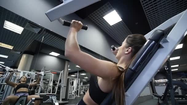 Mujer entrena brazos y hombros en simulador en gimnasio — Vídeo de stock