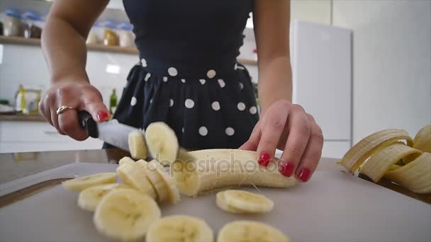 Жінка фрагменти банан на дерев'яні кухню плати домашньої кухні. Приготування їжі в домашніх умовах. Домашня атмосфера на кухні — стокове відео