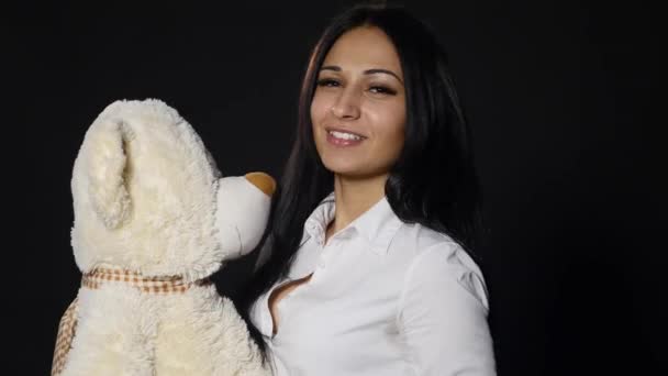 Μια όμορφη κοπέλα αγκαλιές και φιλιά ένα χαριτωμένο αρκουδάκι. Στενή-up shot, στούντιο σε μαύρο φόντο — Αρχείο Βίντεο