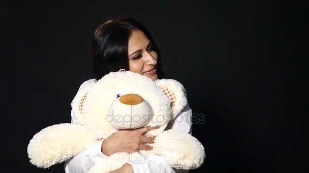 A lovely girl hugs a cute teddy bear. Close-up shot, studio on black background — Stock Video