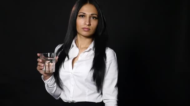 Молодая красивая девушка держит стакан воды на черном фоне — стоковое видео
