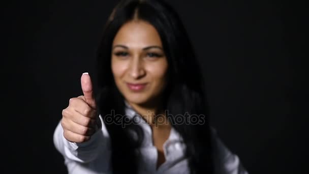 Primer plano retrato de la señora de negocios, de pie sobre fondo de luz pura, sonriendo, en negro fresco especificaciones, muestra el dedo hacia arriba símbolo — Vídeo de stock