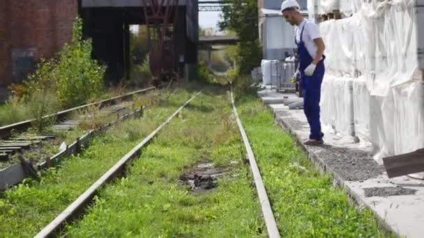 Spoorweg werknemer in wit helm wandelen langs de spoorweg — Stockvideo